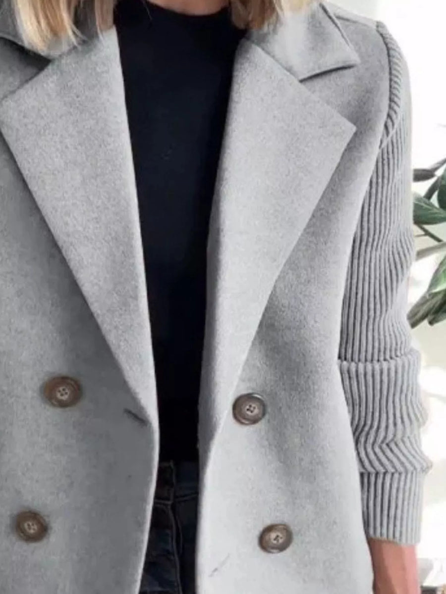 Light gray double-breasted trench coat with knit sleeves and brown buttons.