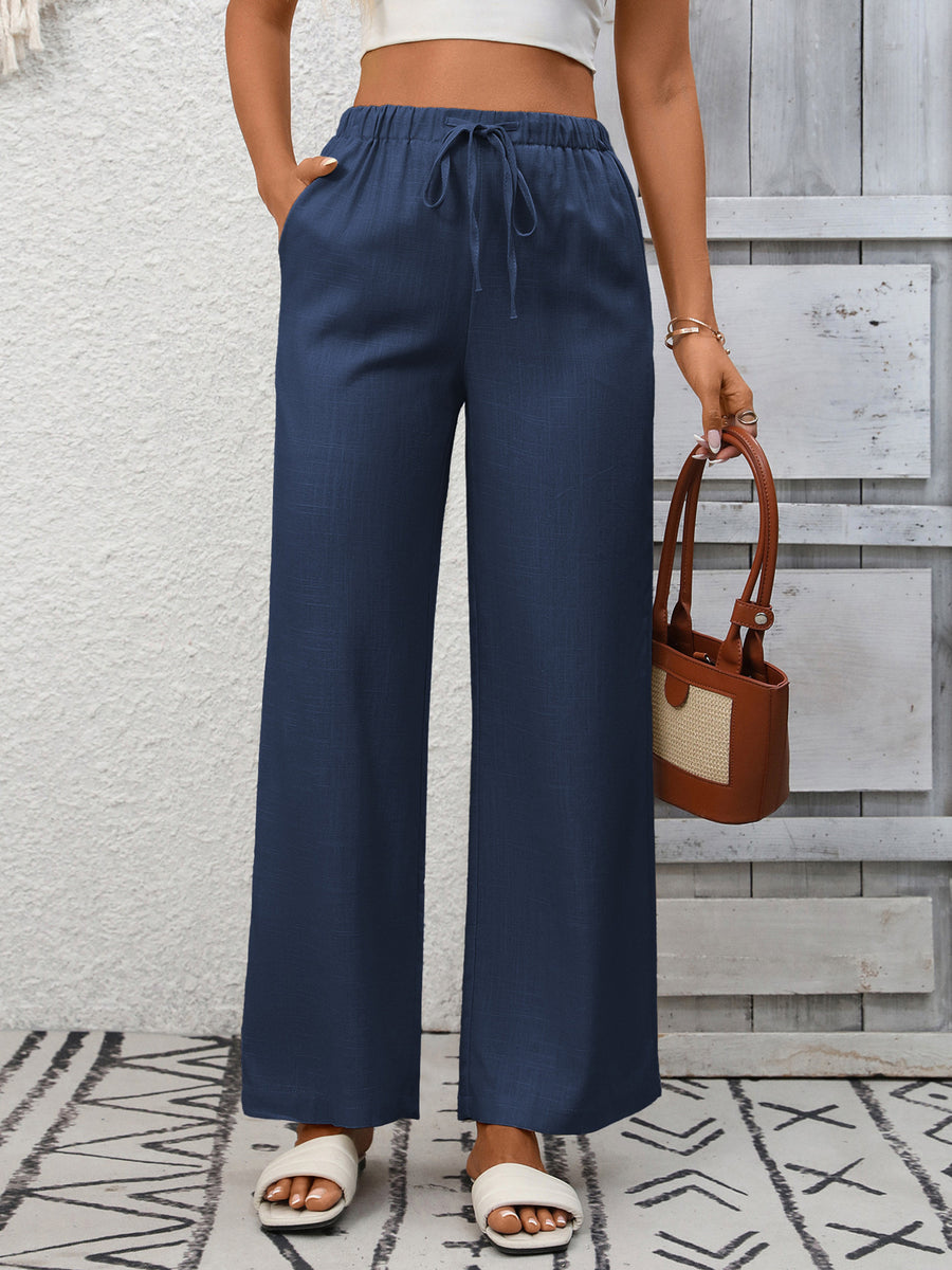 Navy blue wide-leg drawstring pants with pockets, styled with white slides and a brown handbag.