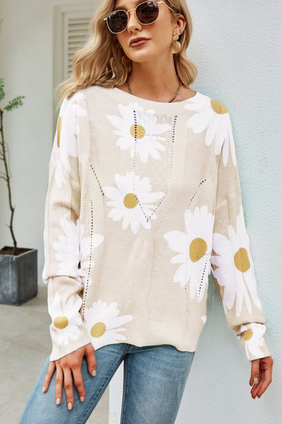 Beige intarsia knit sweater with white daisies, long sleeves, and open knit details.