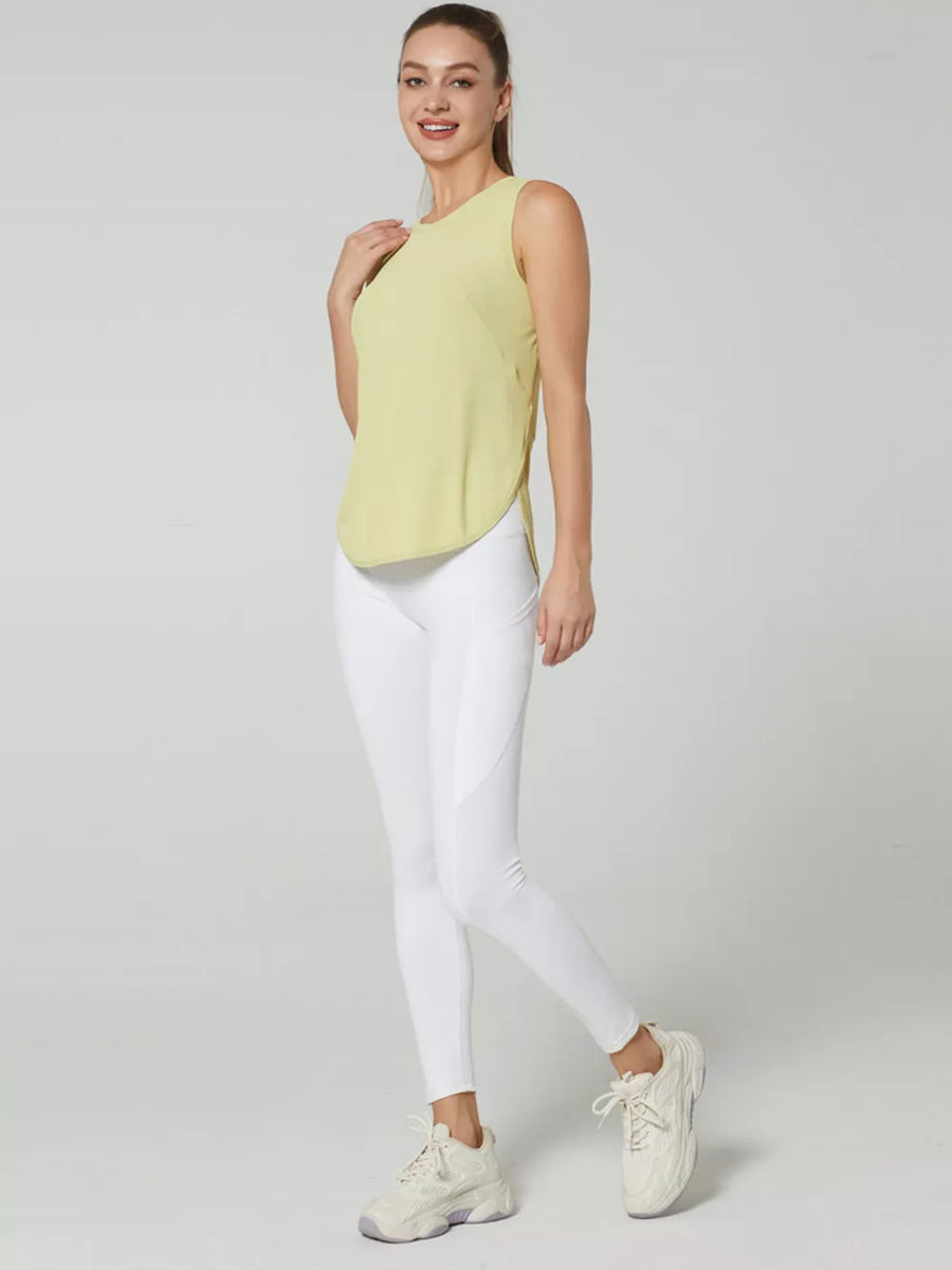 Light yellow sleeveless athletic tank top with curved hem, paired with white leggings.