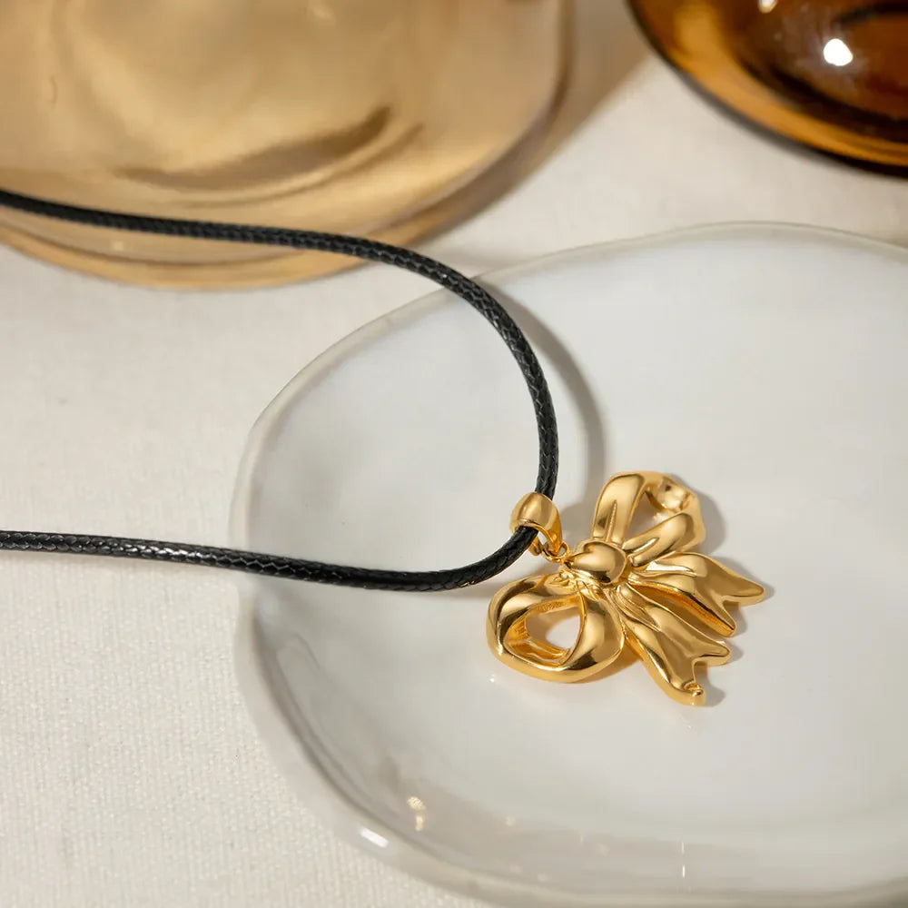 Gold sculptural bow pendant necklace on black wax rope.