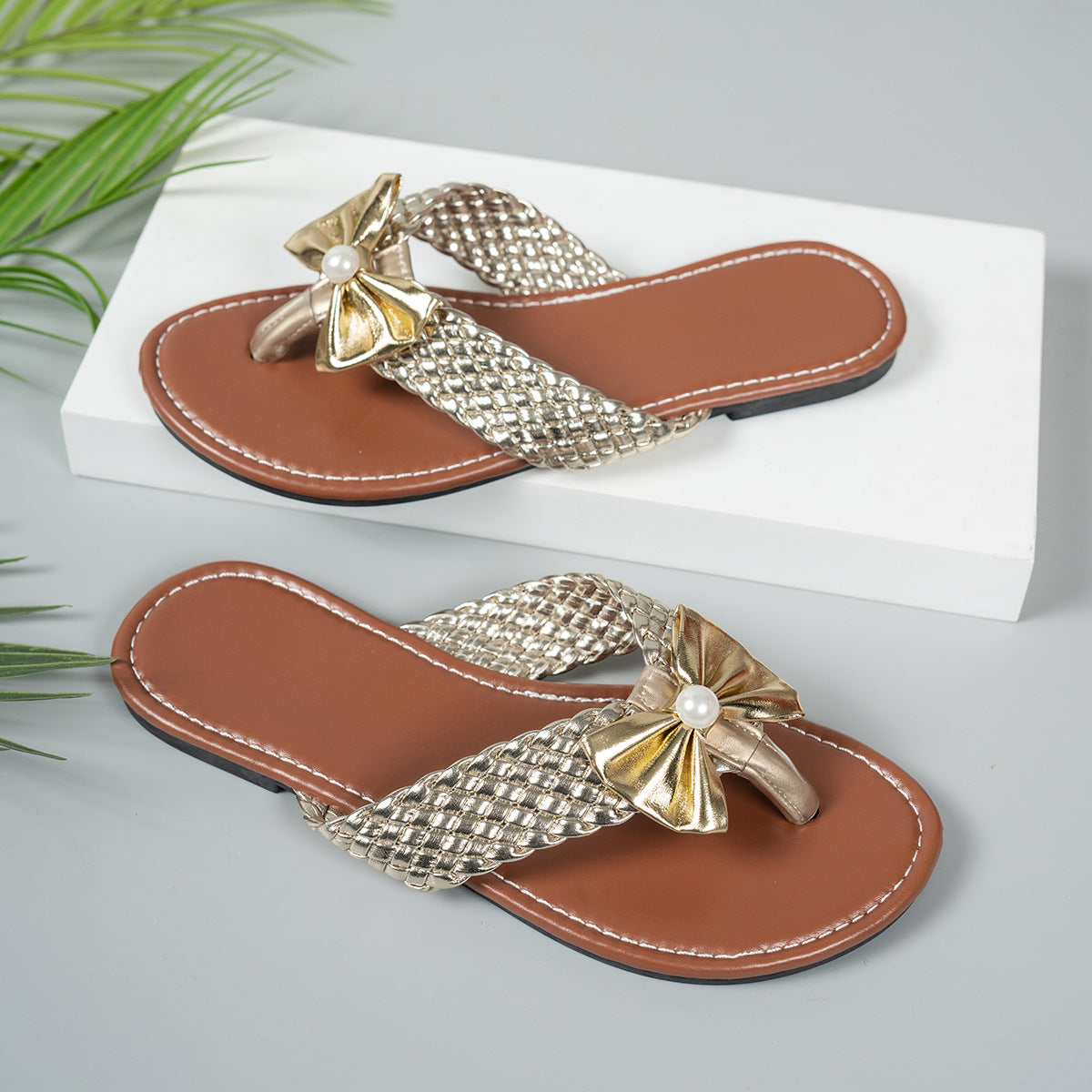 Gold bow embellished flat sandals with woven straps and brown footbed.