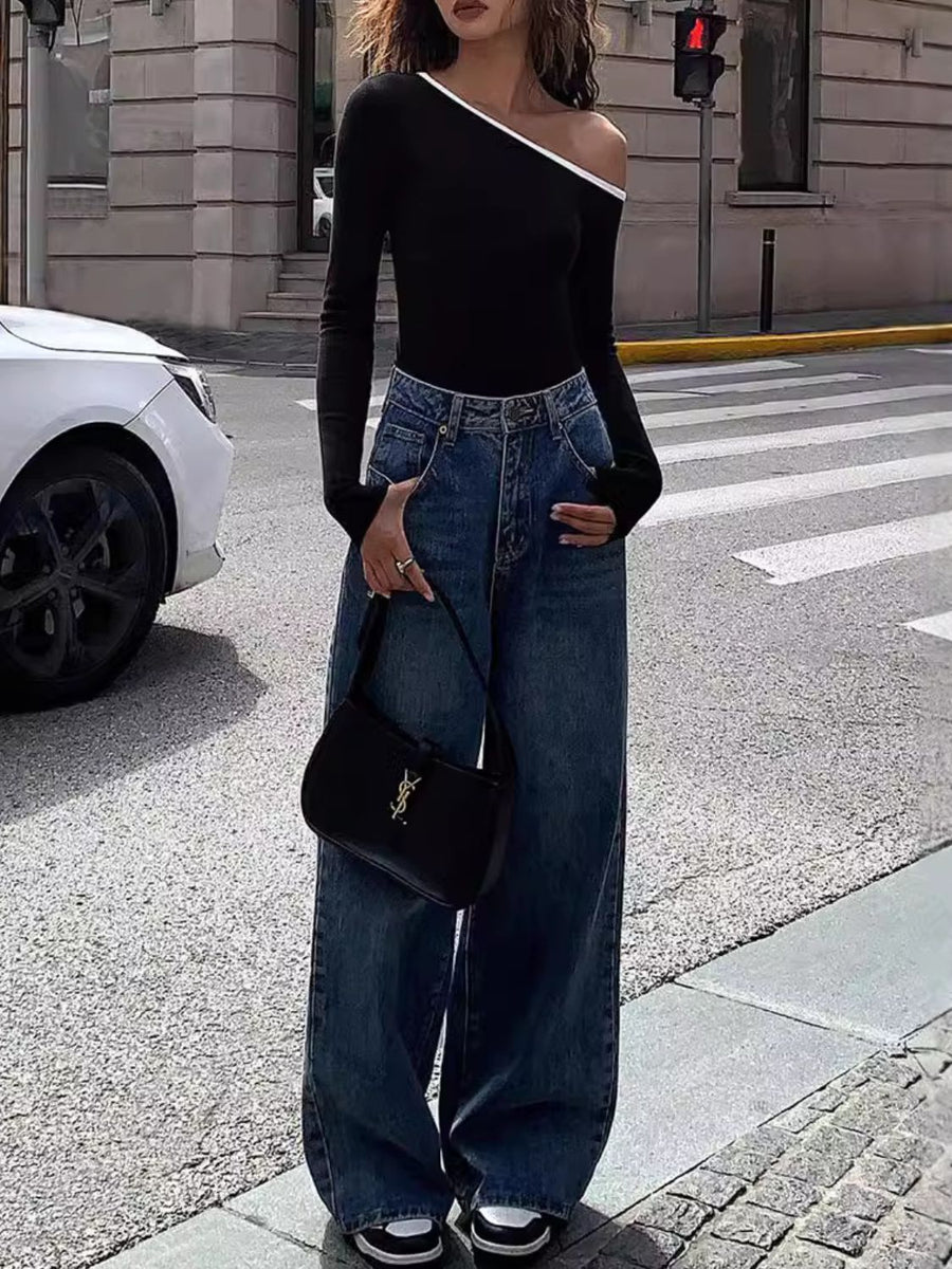 Black off-shoulder ribbed top with contrast trim, long sleeves, paired with wide-leg jeans.