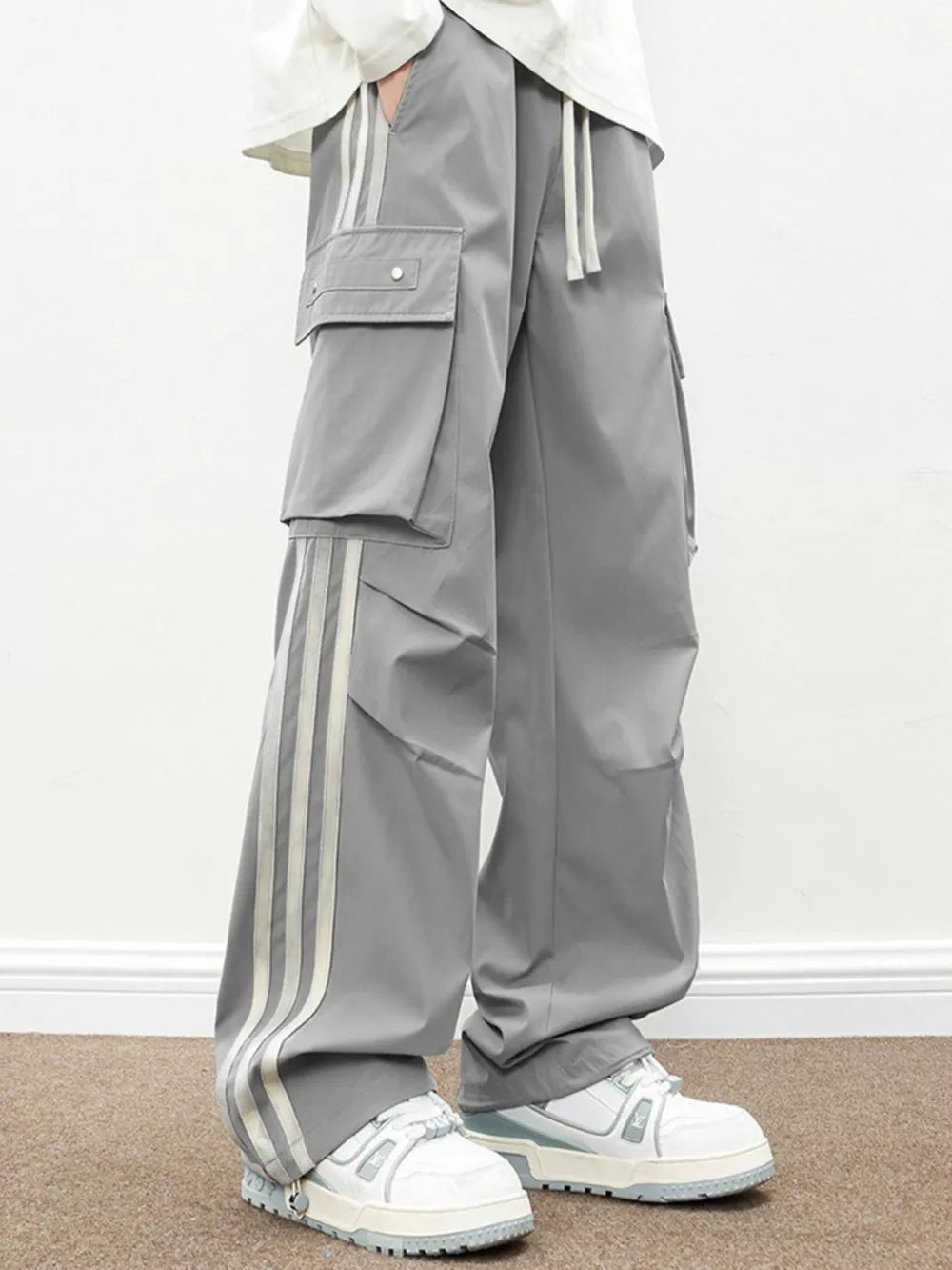 Oversized gray cargo pants with flap pockets and triple stripe detail.