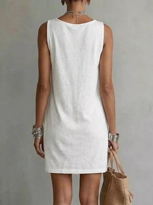 White sleeveless mini dress with a round neckline, styled with bangles and a straw bag.