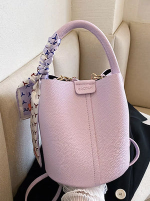 Chic purple bucket crossbody bag with decorative scarf on handle.
