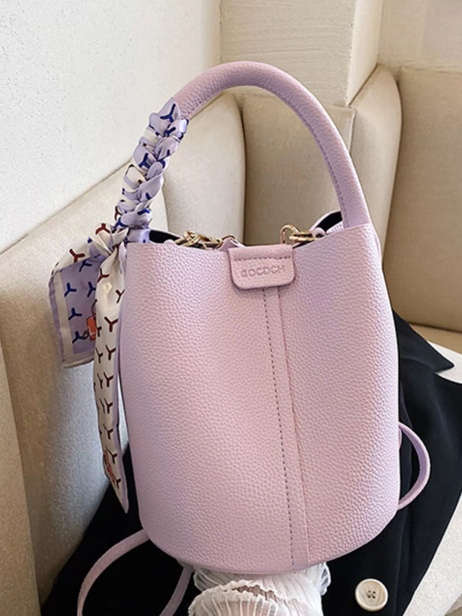 Chic purple bucket crossbody bag with decorative scarf on handle.