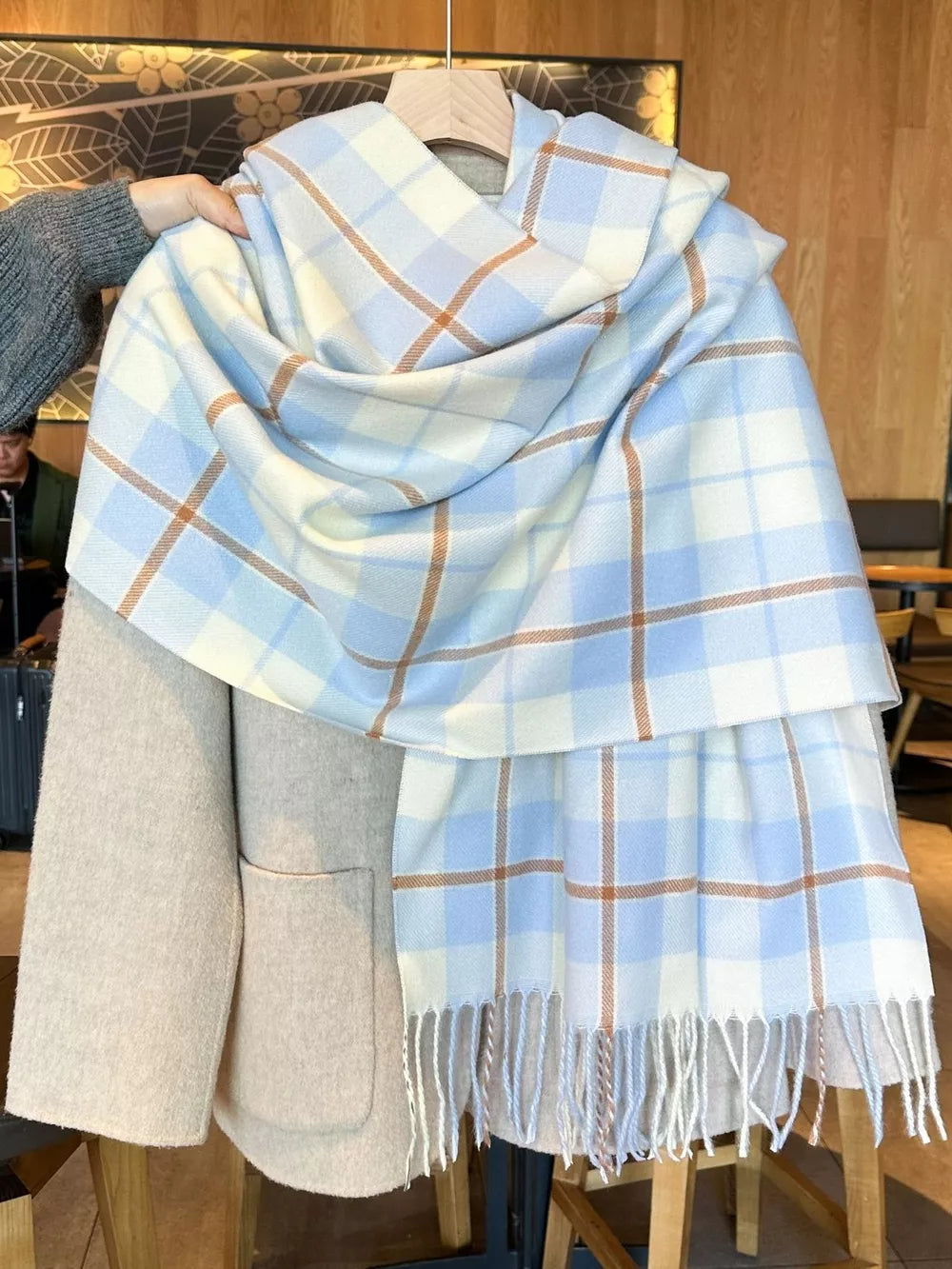 Sky blue plaid fringe scarf with white and tan lines, draped over a tan coat.