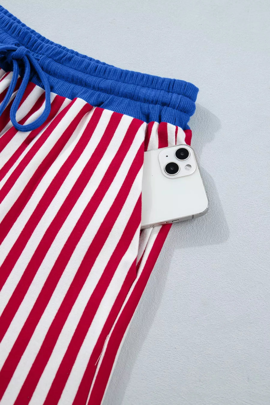 Red and white striped cotton lounge pants with blue drawstring waist and side pocket holding a phone.