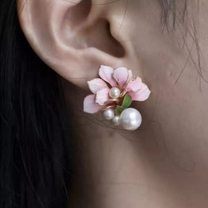 Floral pearl stud earrings in blush pink with pearl accents and green leaf detail.