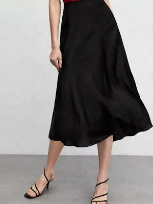 Elegant black high-waisted A-line midi skirt with a flowing silhouette and delicate strappy heels.