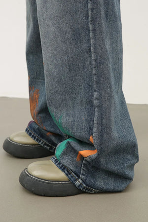 Painterly wide-leg jeans in medium wash denim with artistic orange and green paint splatters.