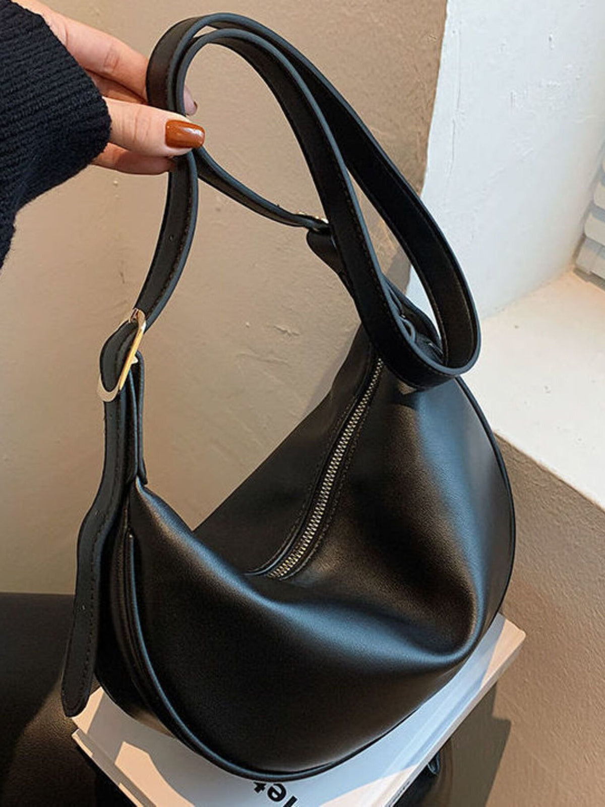 Black pu leather crescent crossbody bag with silver zipper detail and gold buckle.