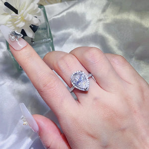Pear-cut halo engagement ring in white metal with a large center stone and pavé band.