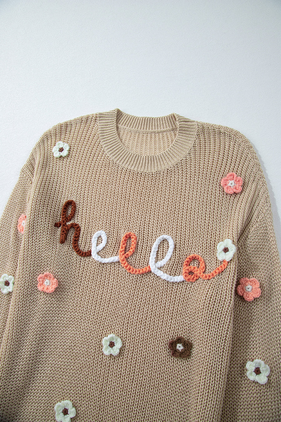 Khaki knit sweater with embroidered "hello" and floral appliques.