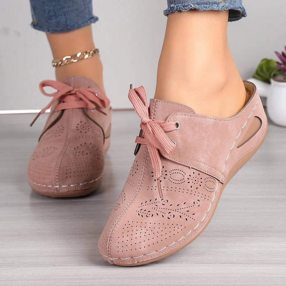 Dusty pink perforated lace-up mule flats with cut-out details and white stitching.