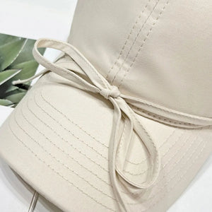 Cream baseball cap with a decorative bow detail and stitched paneling.