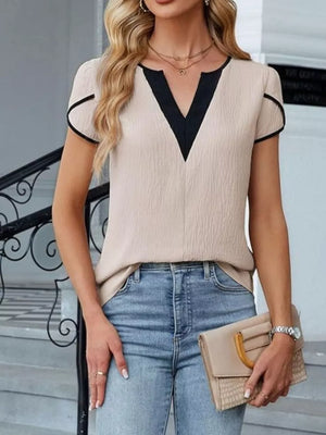 Notched V-neck blouse in beige with black trim and petal sleeves, paired with jeans.