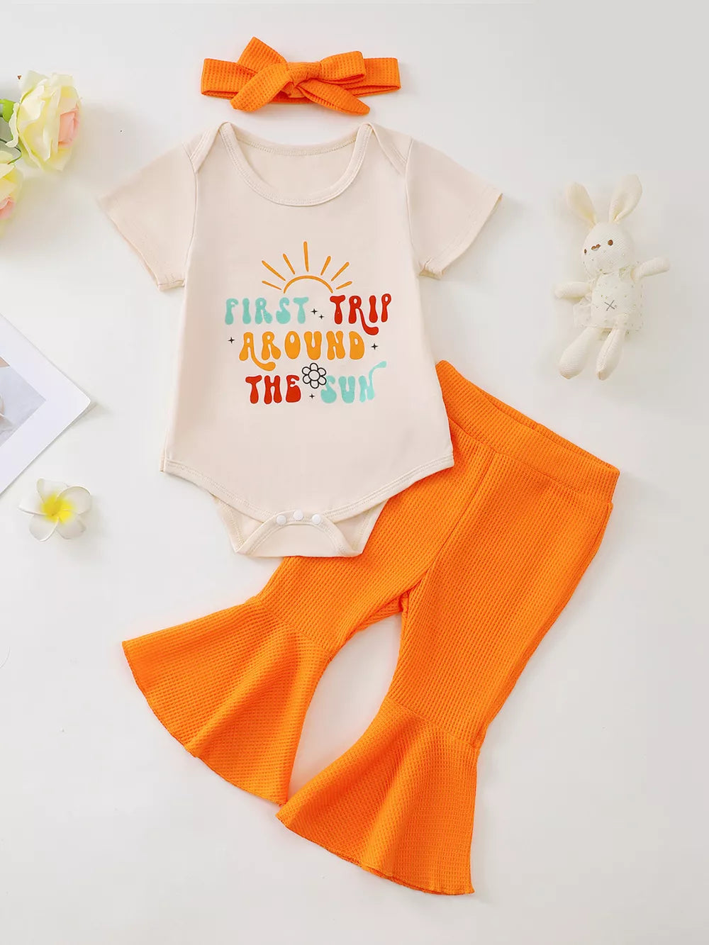 Cream graphic bodysuit with orange bell-bottom pants and headband set.